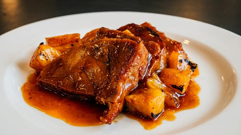 Glazed meat with roasted pineapple chunks and sauce on a white plate.