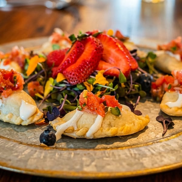 Savory empanadas topped with salsa and cream, garnished with strawberries, blueberries, and microgreens.