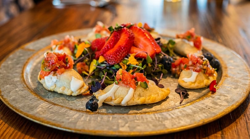 Savory empanadas topped with salsa and cream, garnished with strawberries, blueberries, and microgreens.